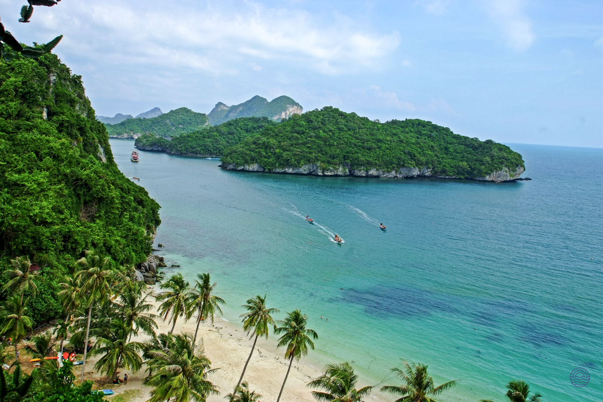Overhead view of a beautiful Thai island bay with a sandy beach, palm trees, and boats.