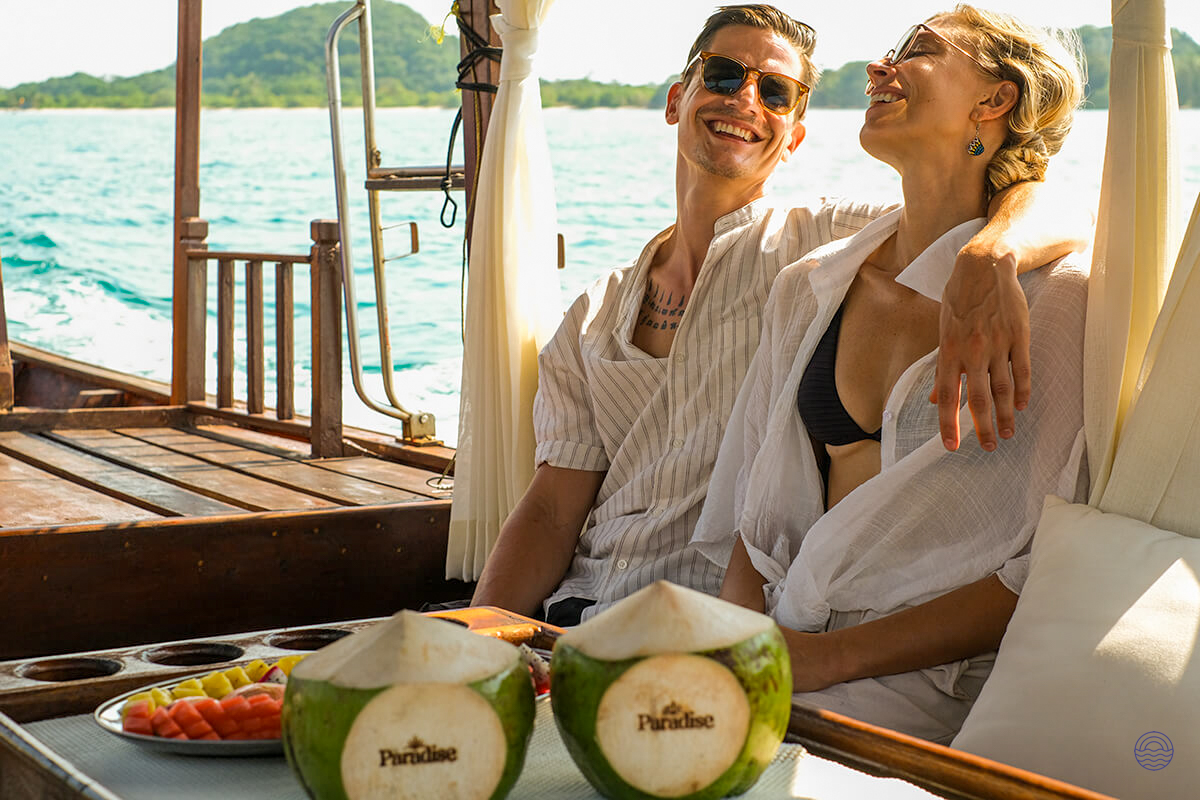 A happy couple enjoys fresh coconuts and fruit on a luxurious longtail boat in Koh Samui.