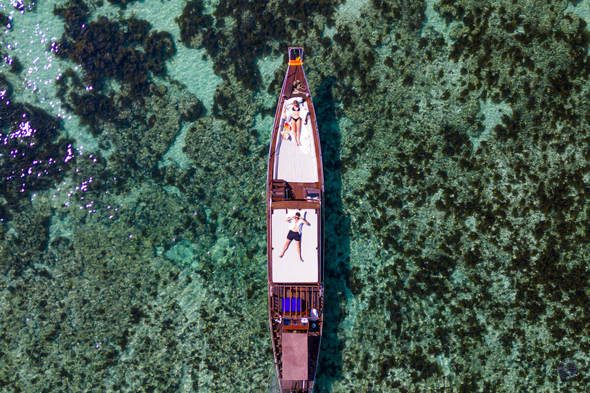 Two people relax on a luxurious longtail boat over clear turquoise waters in Koh Samui.