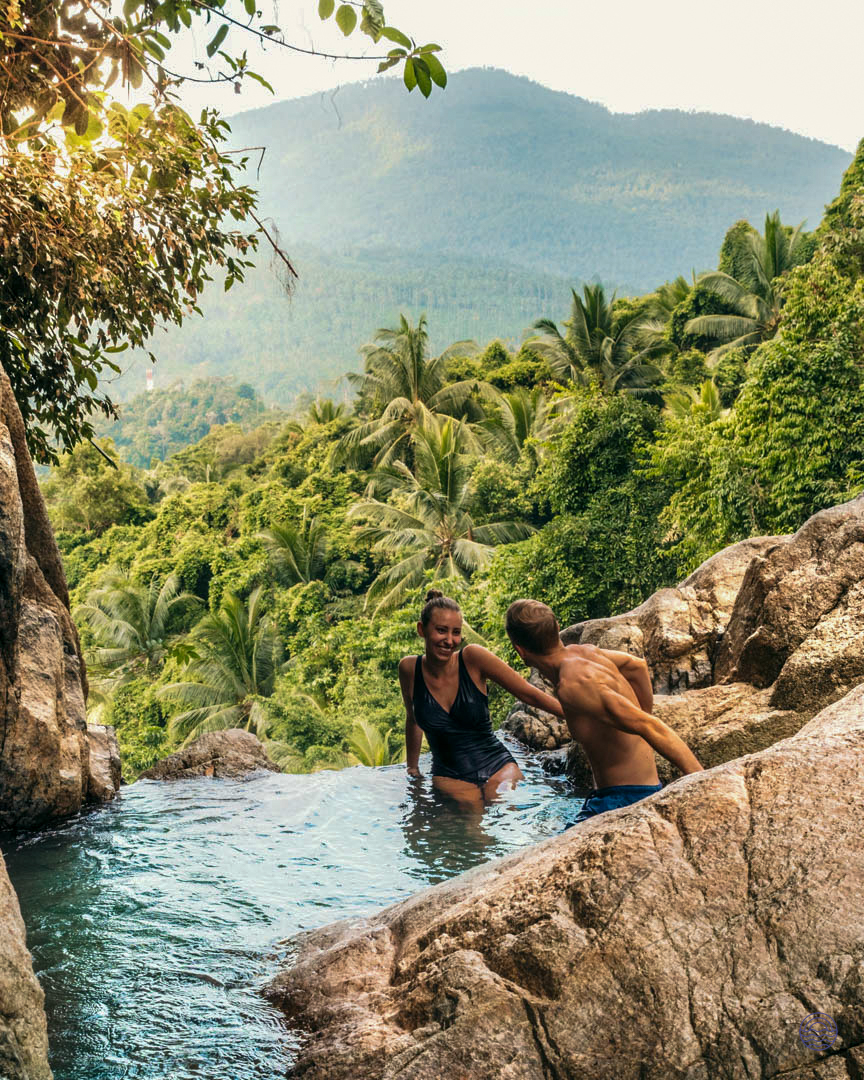 A happy couple enjoys a refreshing swim in a natural pool overlooking the lush Koh Samui jungle.