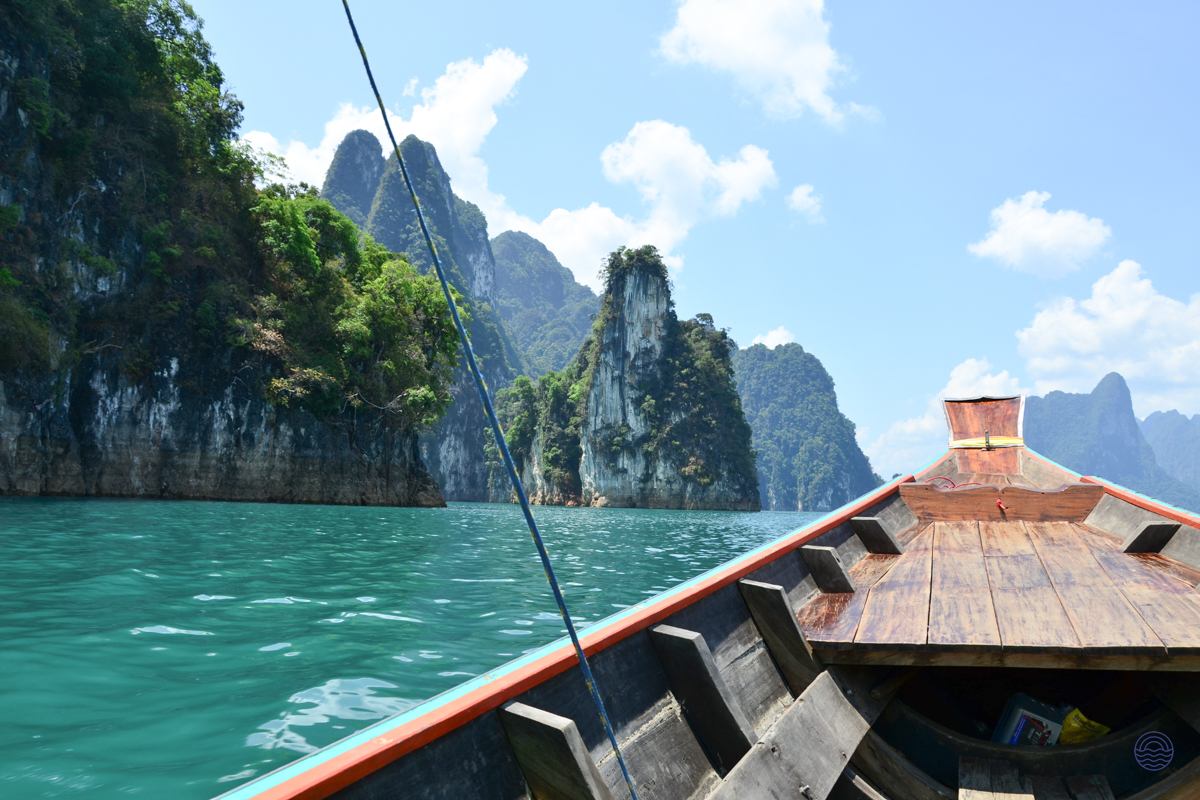 A longtail boat glides through the tranquil turquoise waters of Khao Sok, surrounded by majestic limestone karsts.