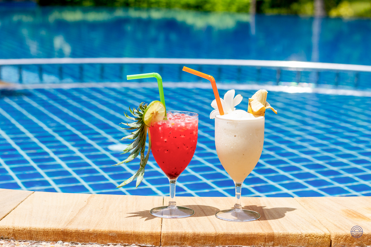 Two refreshing tropical cocktails sit by a sparkling blue swimming pool, ready for relaxation.