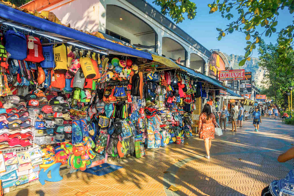 Shoppers explore a vibrant outdoor market in Krabi, browsing colorful clothes and local souvenirs.