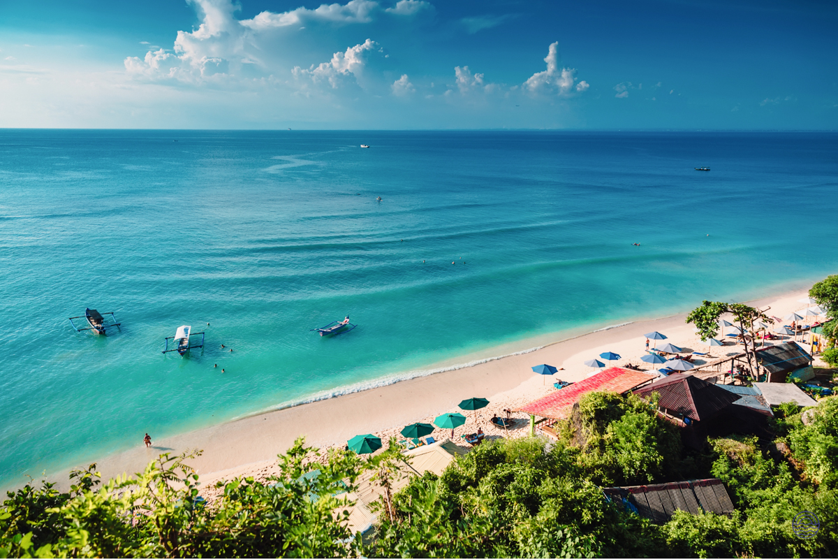 Stunning aerial view of a vibrant turquoise beach in Phuket with boats and green umbrellas.