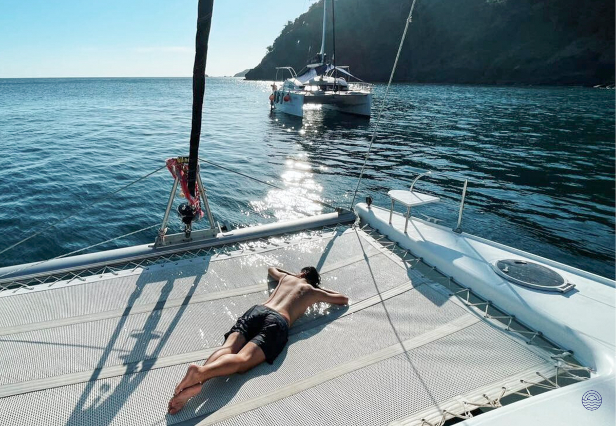 A man unwinds on a catamaran's netting, enjoying the sunny cruise off Phuket in the Andaman Sea.