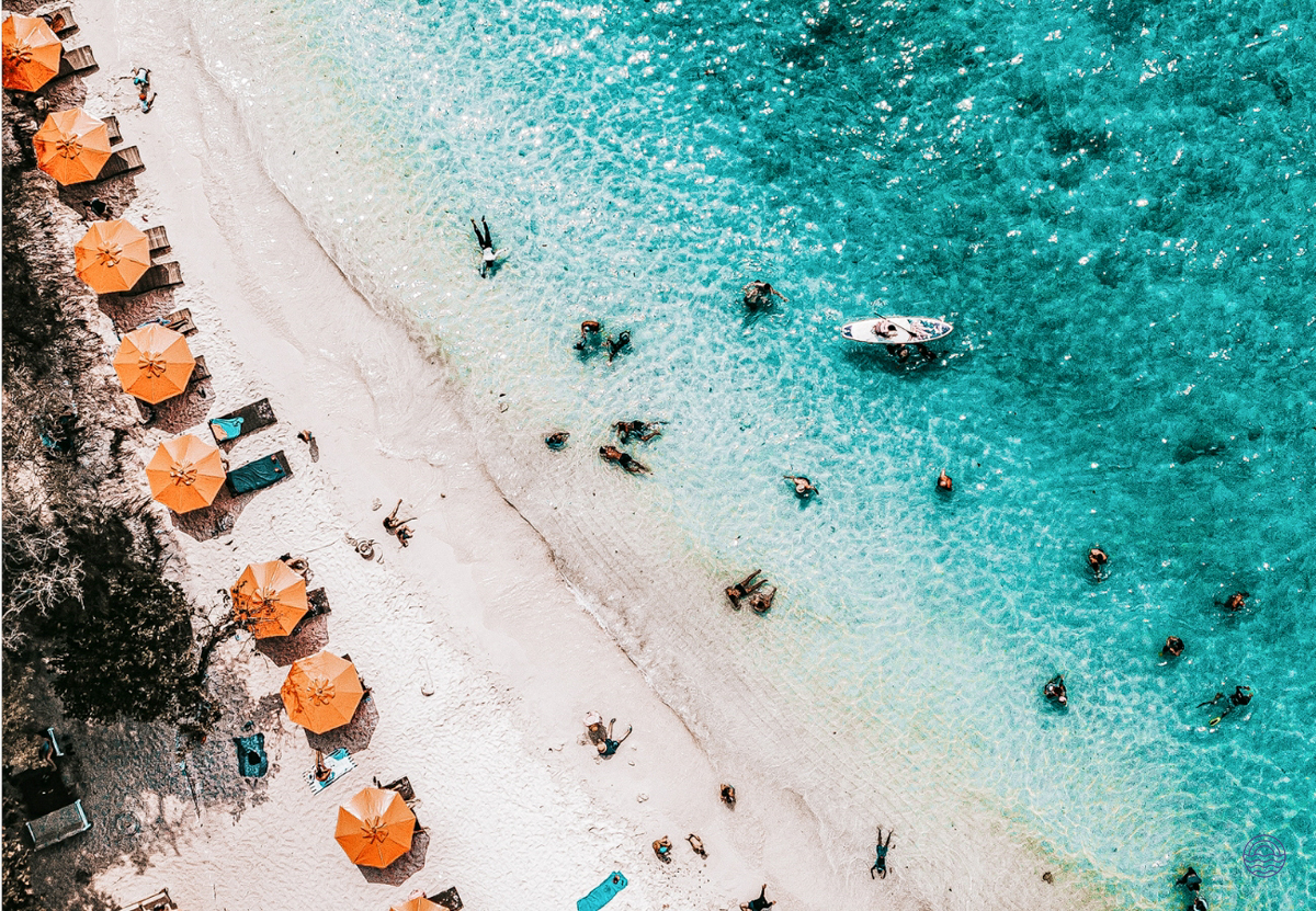 Many people enjoying the clear turquoise waters and white sand beach with orange umbrellas in Phuket.