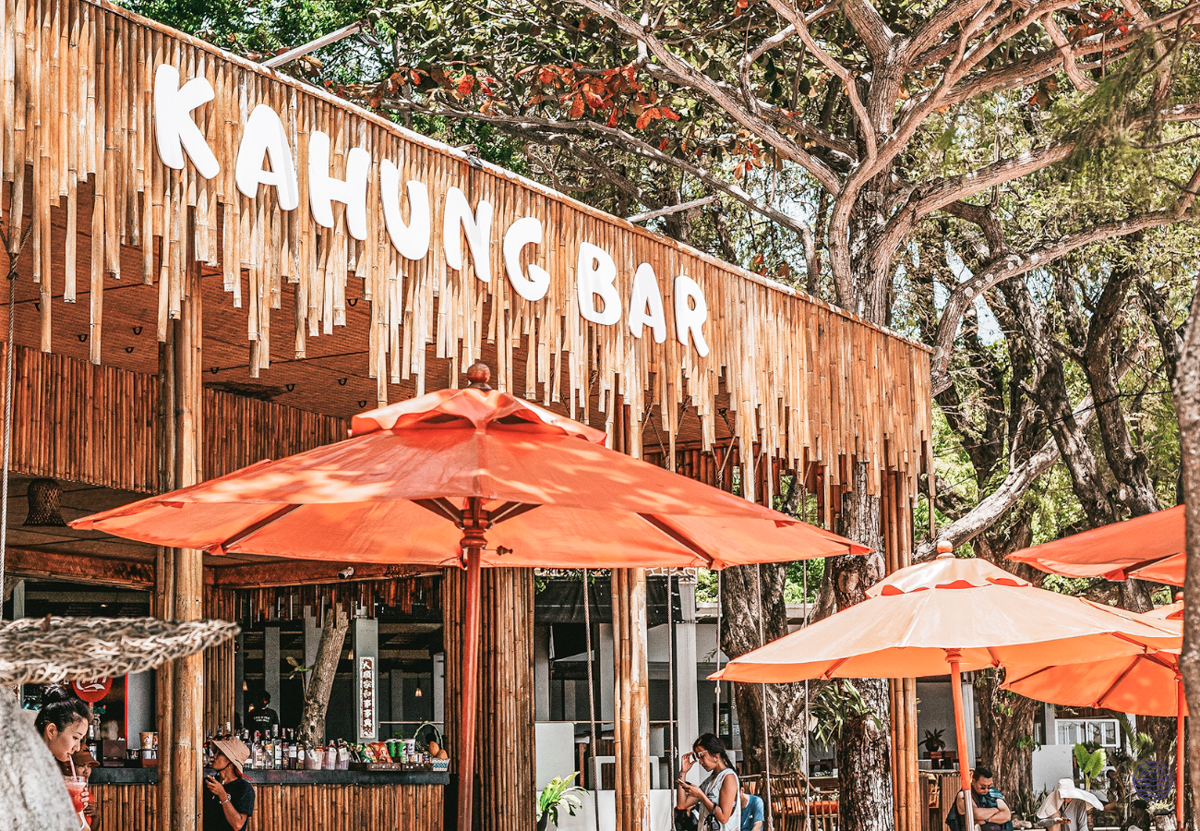 Guests relaxing under orange umbrellas at the rustic Kahung Bar, a tropical haven in Phuket.