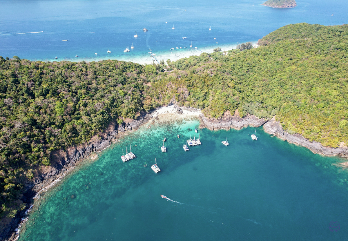 Catamarans and boats anchored in a serene turquoise bay surrounded by lush green islands near Phuket.