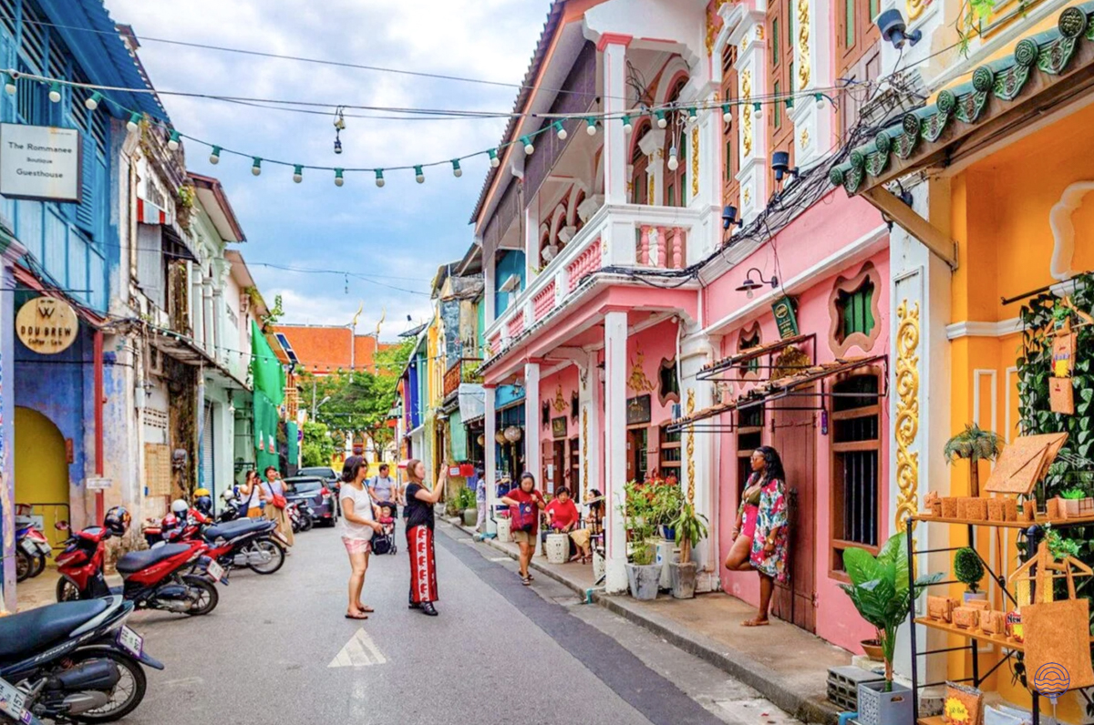 Tourists explore the vibrant, colorful Sino-Portuguese architecture of Phuket Old Town on a sunny day.
