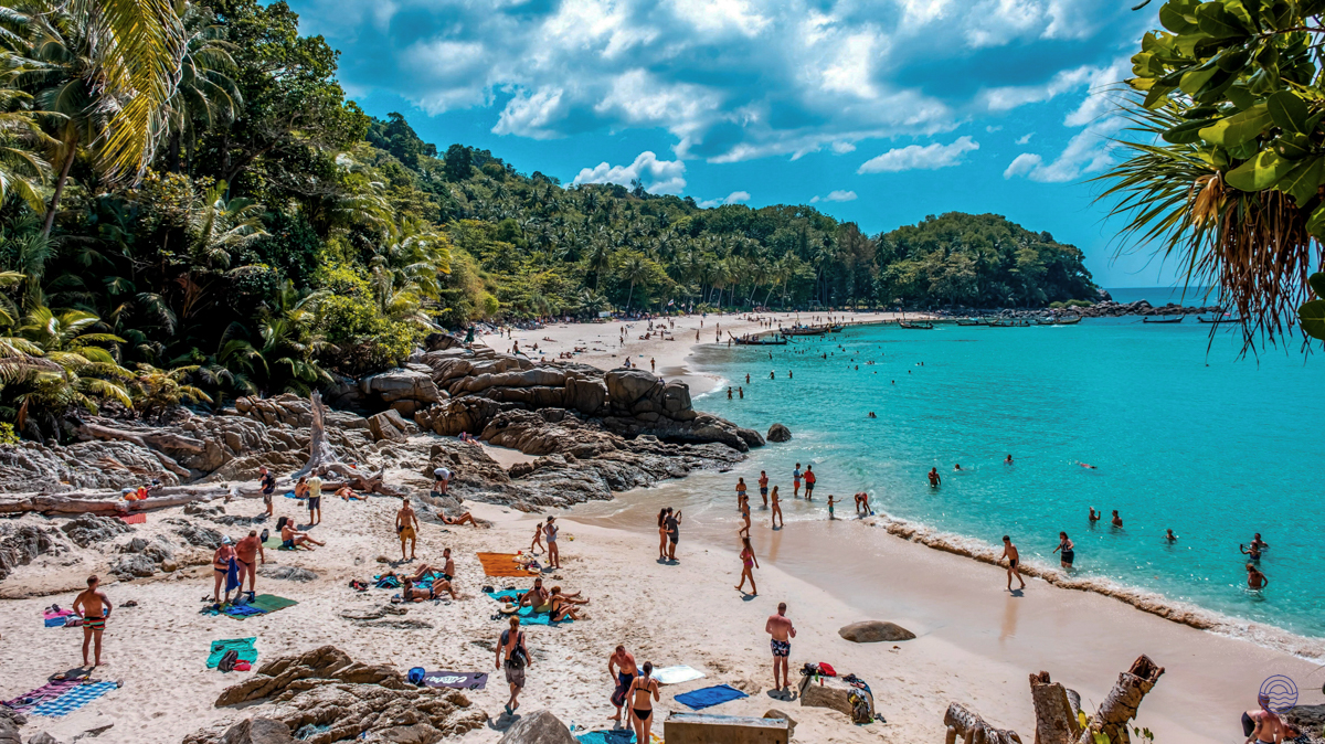 Many people relax and swim on a sunny white sand beach with clear blue water in Phuket.