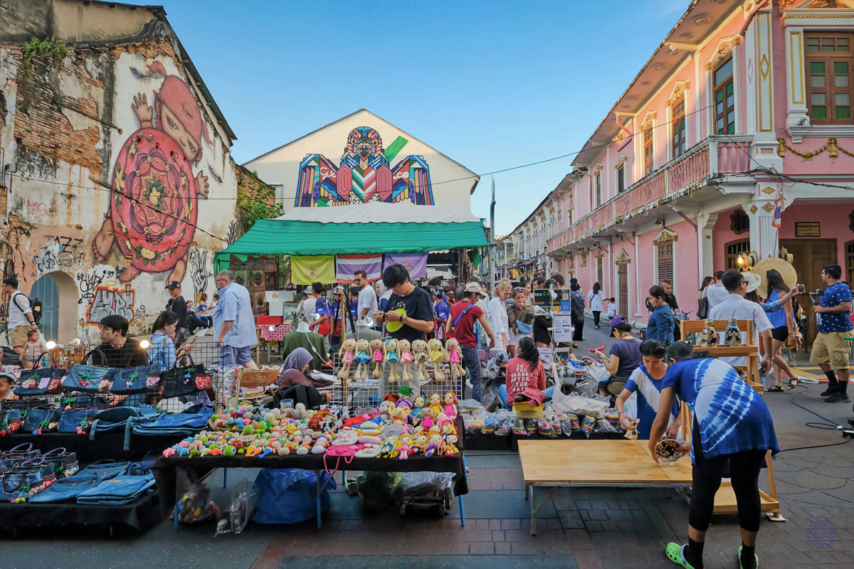 A bustling street market in Phuket Old Town with many people browsing colorful stalls.