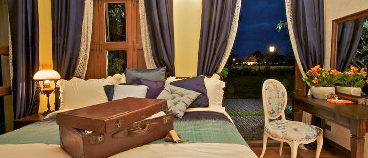 A charming hotel room in Bangkok at night, featuring a bed, open suitcase, and elegant decor.