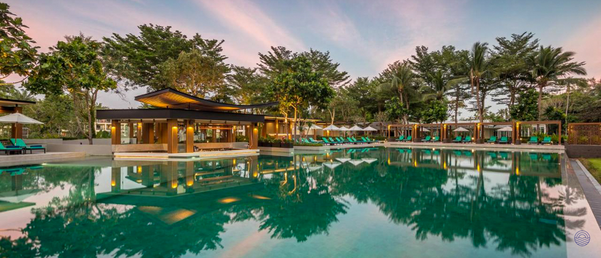 Luxurious resort swimming pool reflecting a pink sunset sky, surrounded by lush trees in Krabi.