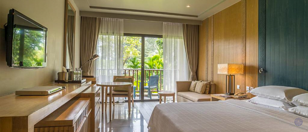 Relaxing hotel room in Krabi with a comfortable bed, sofa, and balcony overlooking tropical trees.