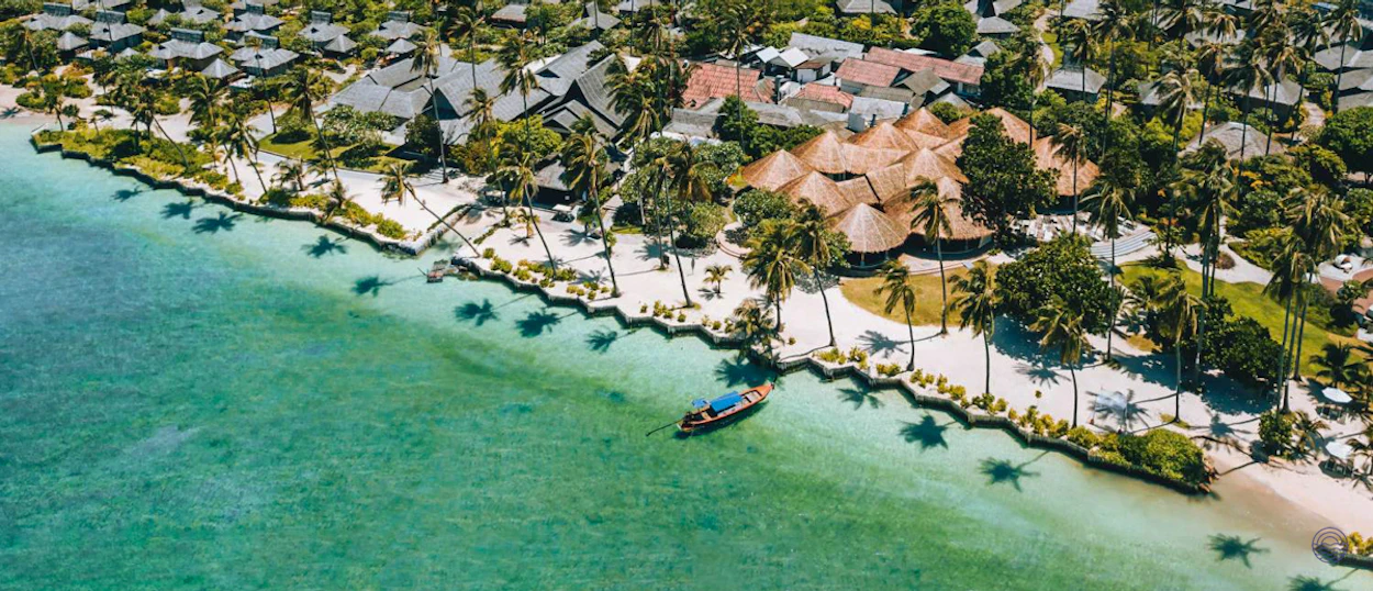 Beautiful tropical resort with palm trees and a longtail boat in turquoise waters of Koh Phi Phi.