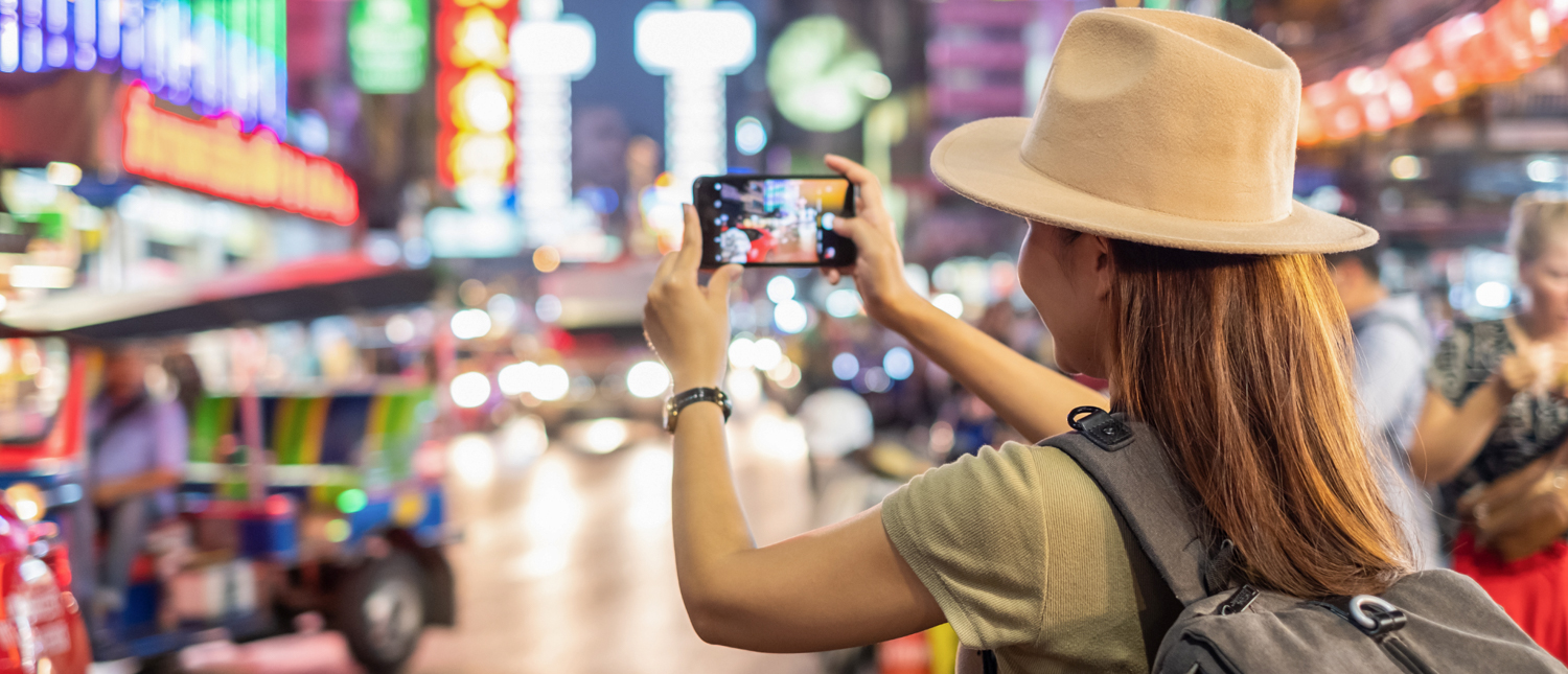 A traveler photographs the colorful neon signs and busy street life of Bangkok at night.