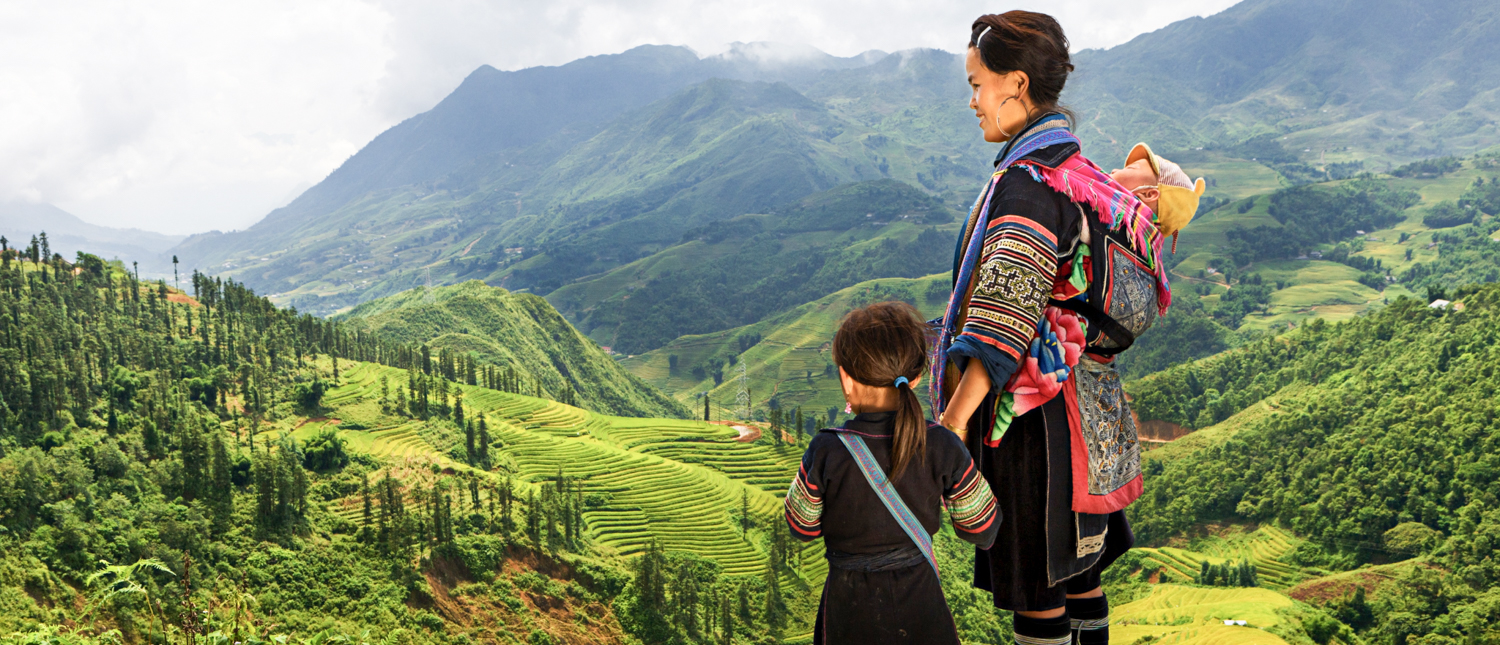 A Hmong woman and child in traditional clothing admire the lush green mountains of Chiang Mai.