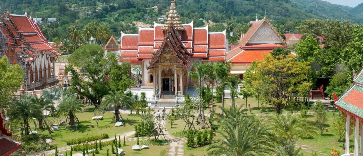 An ornate Thai temple complex with red roofs and golden spires amidst lush green gardens in Chiang Mai.
