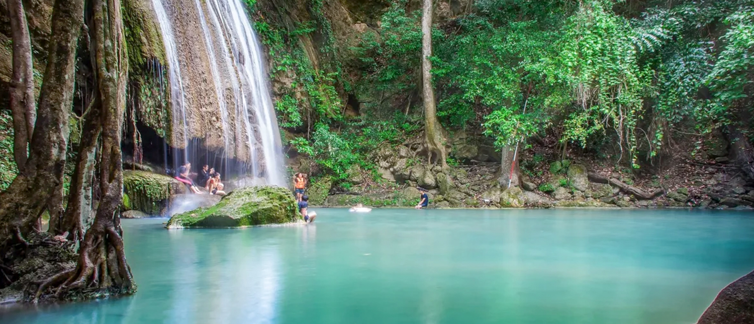 People swim and relax in the emerald-green pools of Erawan Waterfalls, Thailand, surrounded by lush jungle.