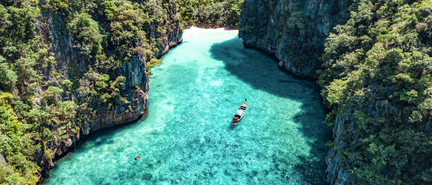 A longtail boat floats on clear turquoise water between lush green cliffs in Phi Phi Islands.
