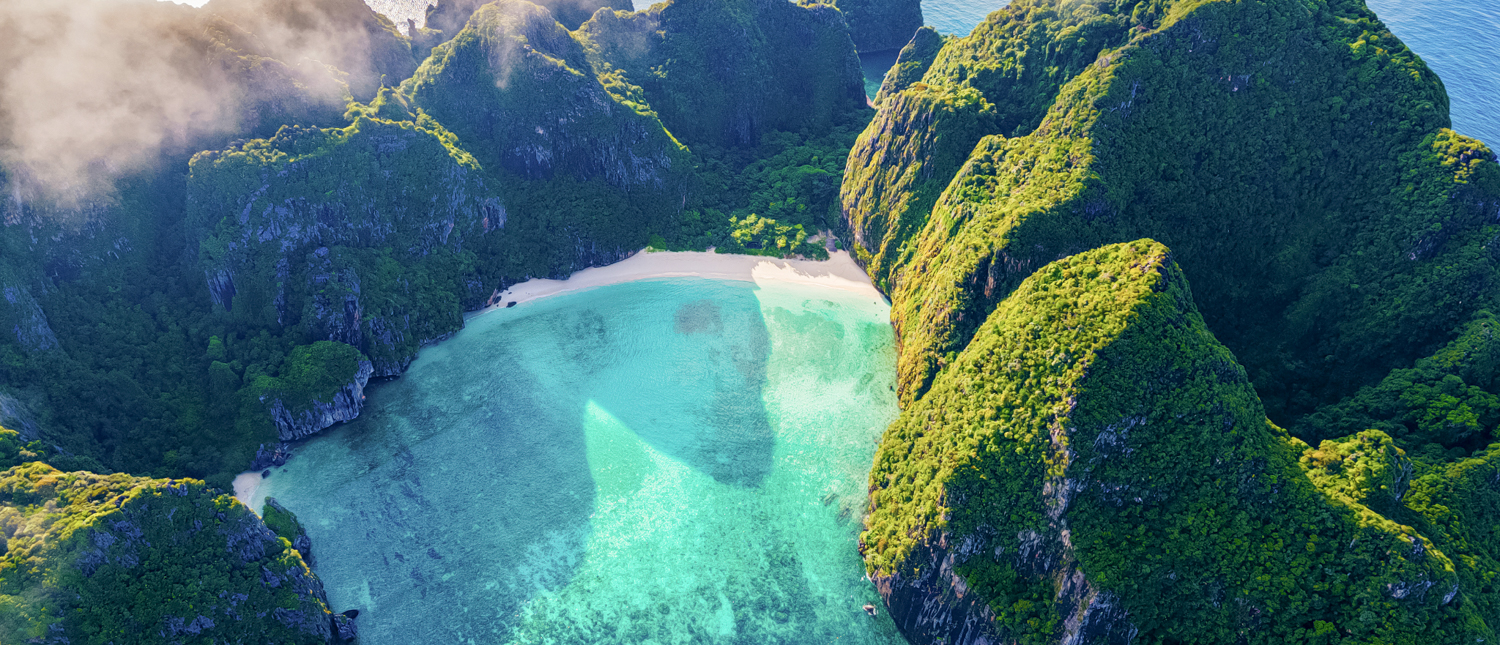 Aerial view of Maya Bay in Phi Phi Islands, Thailand, with turquoise water and towering green cliffs.