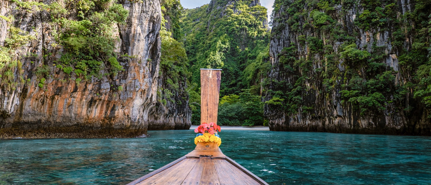 A decorated longtail boat navigates the serene turquoise waters of Phi Phi Islands, flanked by majestic green cliffs.