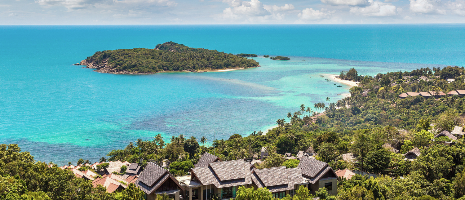 Stunning view of Koh Samui's tropical coastline with clear turquoise waters and villas among green trees.