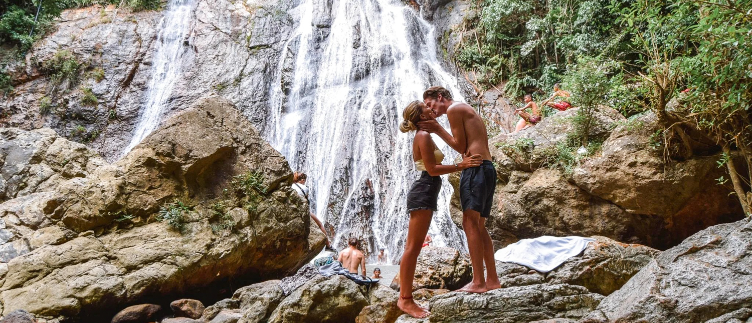 A romantic couple kisses on rocks at a beautiful waterfall on Koh Samui.