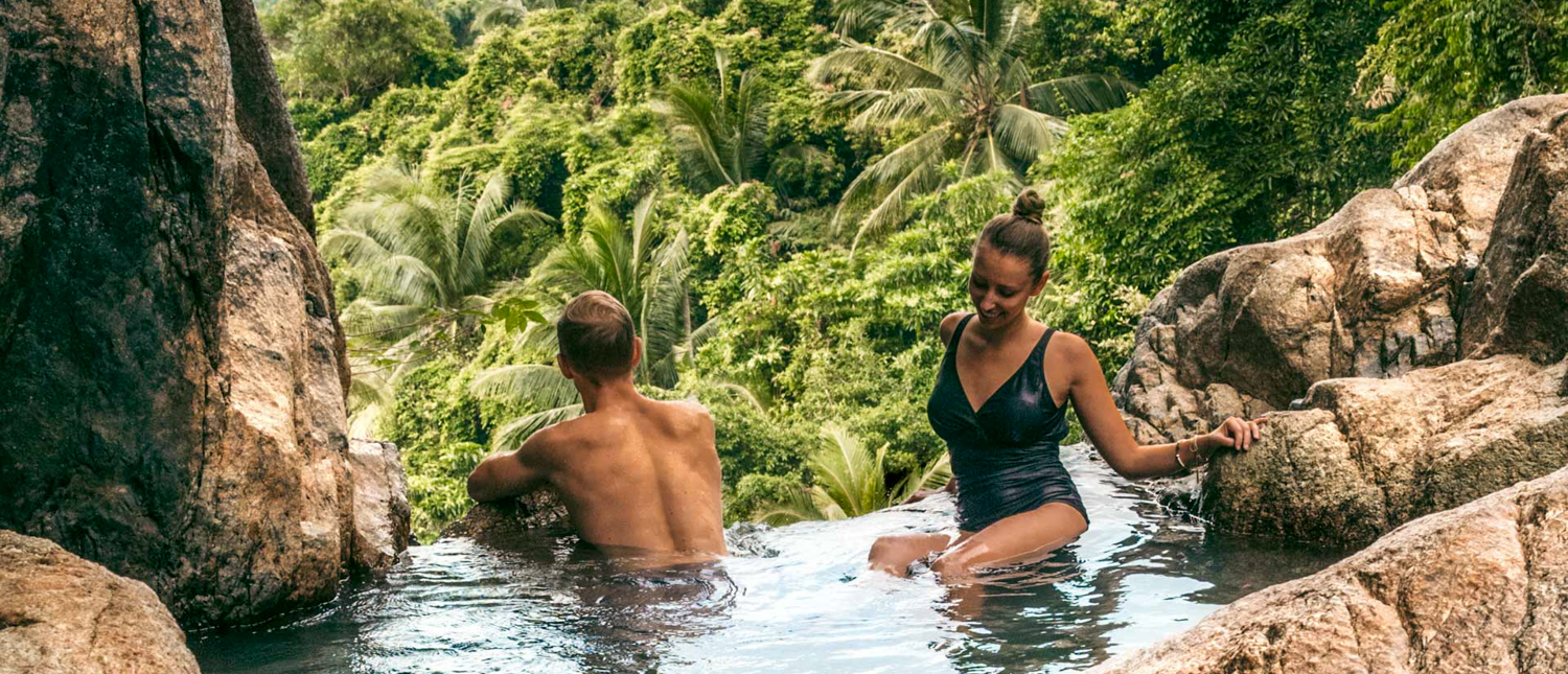 A couple relaxes in a natural rock pool surrounded by lush tropical jungle on Koh Samui.