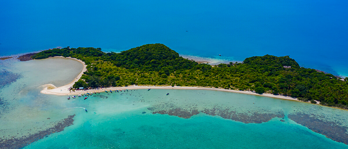 Stunning aerial view of Koh Madsum, a lush green island with white sand and clear turquoise water.