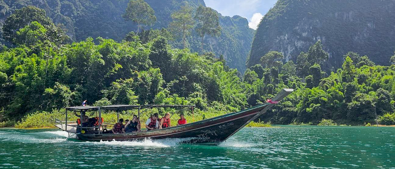 Tourists enjoy a scenic longtail boat ride on turquoise water surrounded by lush limestone karsts in Khao Sok.