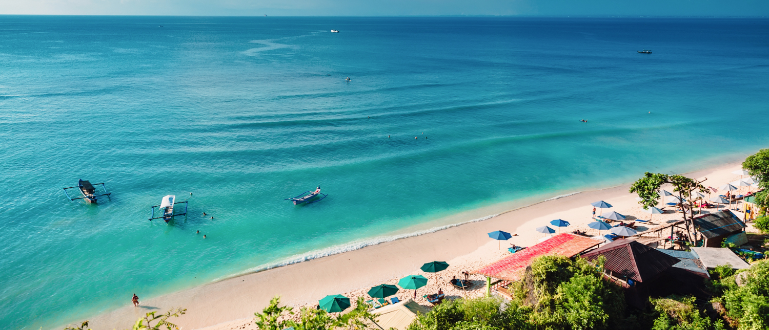 Overhead view of a beautiful Phuket beach with calm turquoise water, boats, and beach umbrellas.