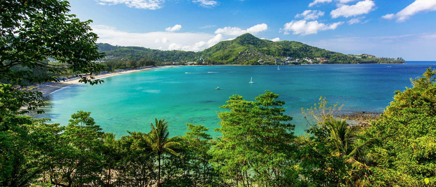 Stunning panoramic view of a tropical beach with turquoise water and lush green mountains in Phuket.