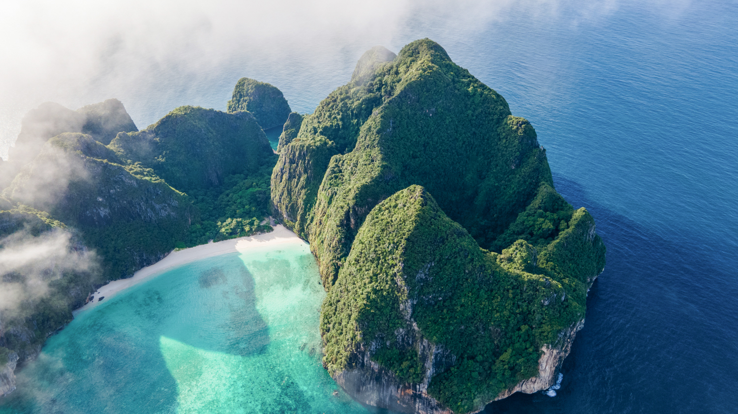 Majestic green limestone cliffs, a white sand beach, and turquoise waters at Koh Phi Phi, Thailand.