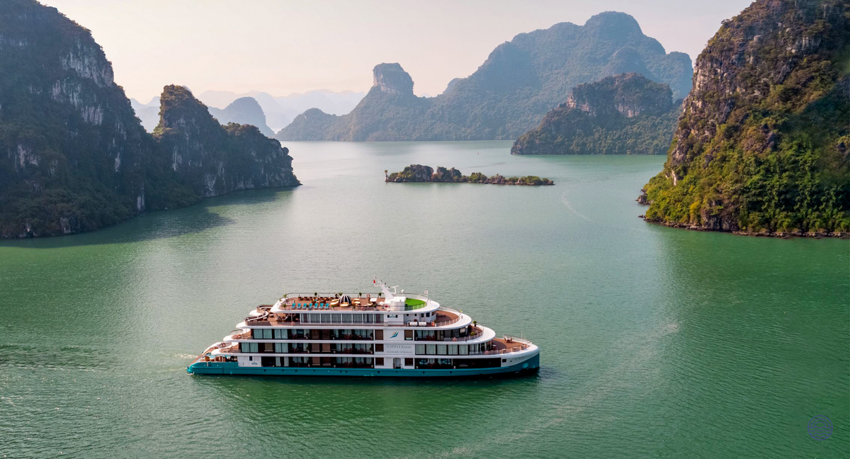 A luxury cruise ship glides through the serene emerald waters of Halong Bay, surrounded by towering karsts.