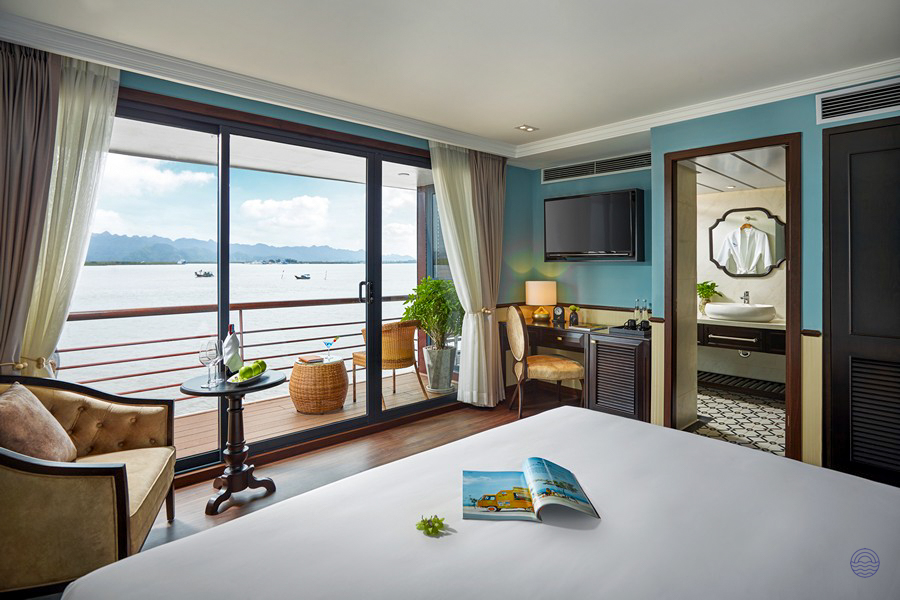 A spacious cruise cabin with a comfortable bed and private balcony offering stunning views of Halong Bay.