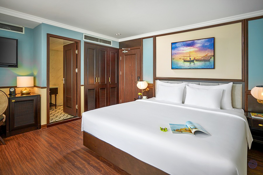 A luxurious Capella Cruise cabin in Halong Bay, with a large bed and elegant wooden furnishings.