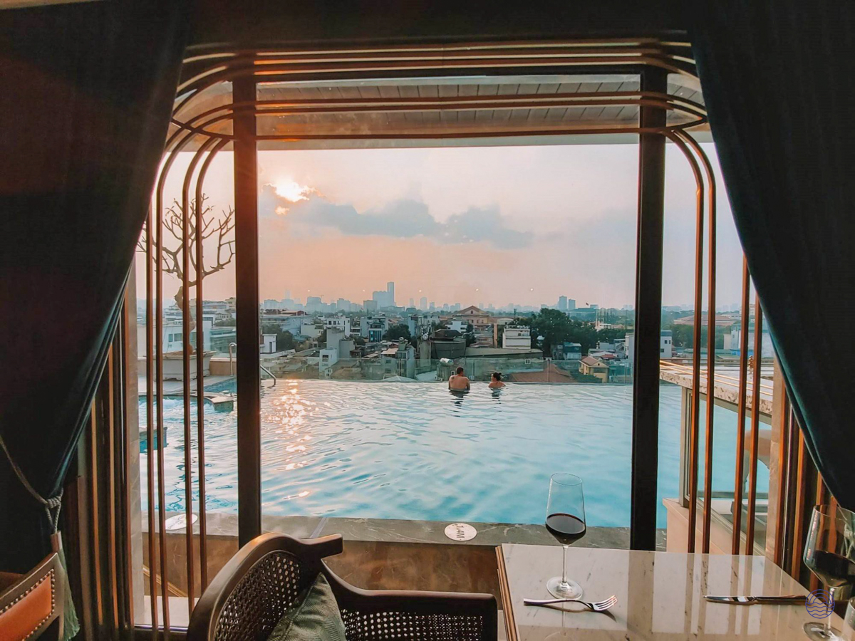 Guests relax in a luxurious rooftop infinity pool overlooking the Hanoi cityscape at sunset.