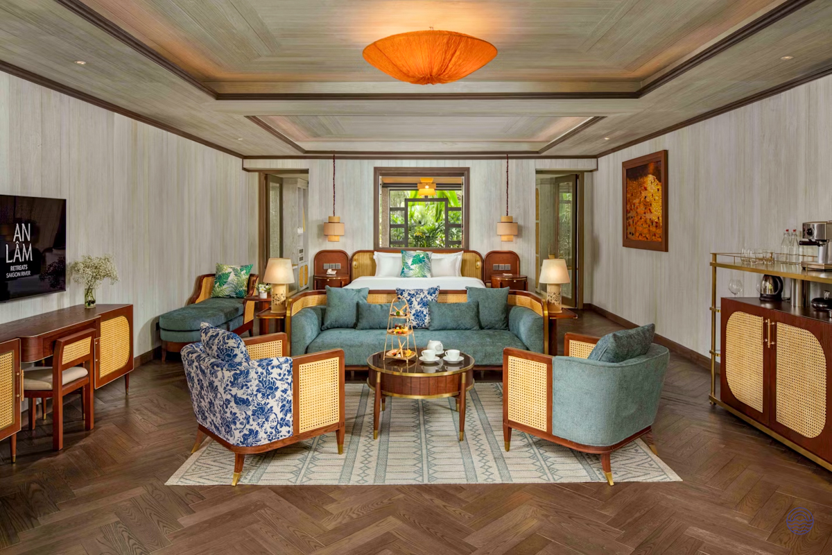 Luxurious hotel suite with a large bed, blue sofa, and elegant wooden furniture on herringbone floors.