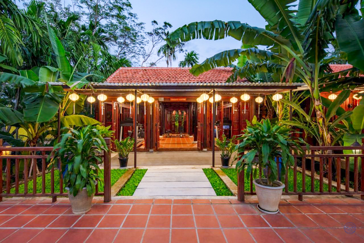 An inviting traditional hotel entrance in Hoi An, beautifully lit by lanterns and surrounded by tropical plants.
