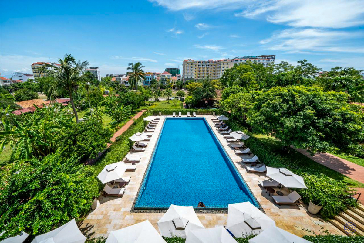 An inviting outdoor swimming pool with lounge chairs and umbrellas surrounded by lush greenery in Hoi An.