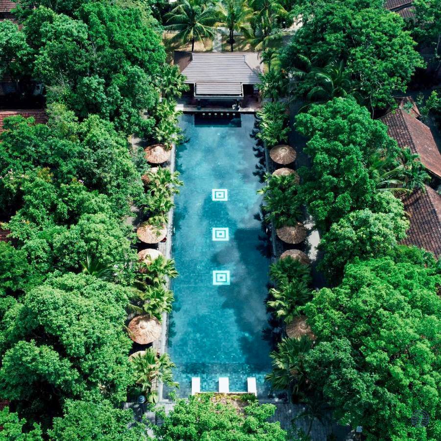 An aerial view of a serene resort swimming pool surrounded by lush tropical trees in Hue.