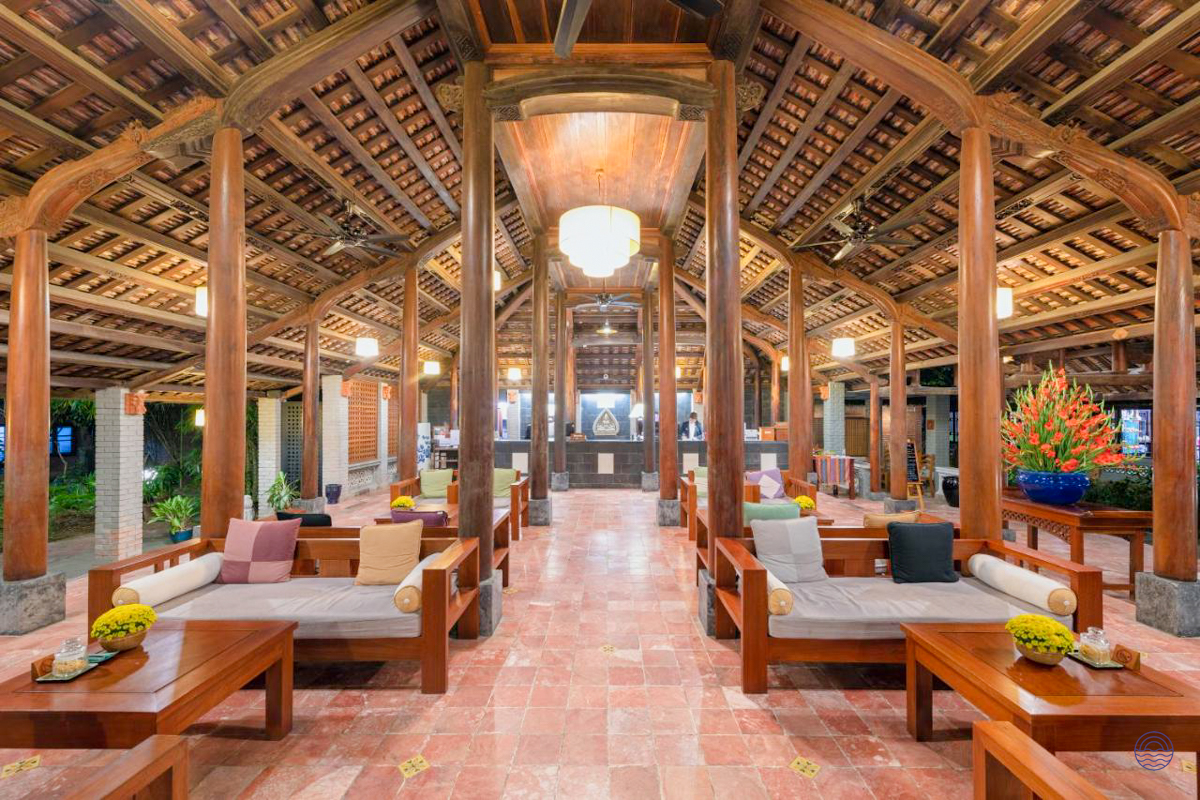Elegant open-air lobby of a Hue resort, featuring traditional wooden ceilings, comfortable seating, and floral decor.