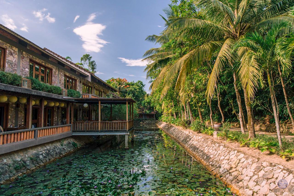 Tropical resort architecture in Hue, featuring a serene canal with lily pads and tall palm trees.