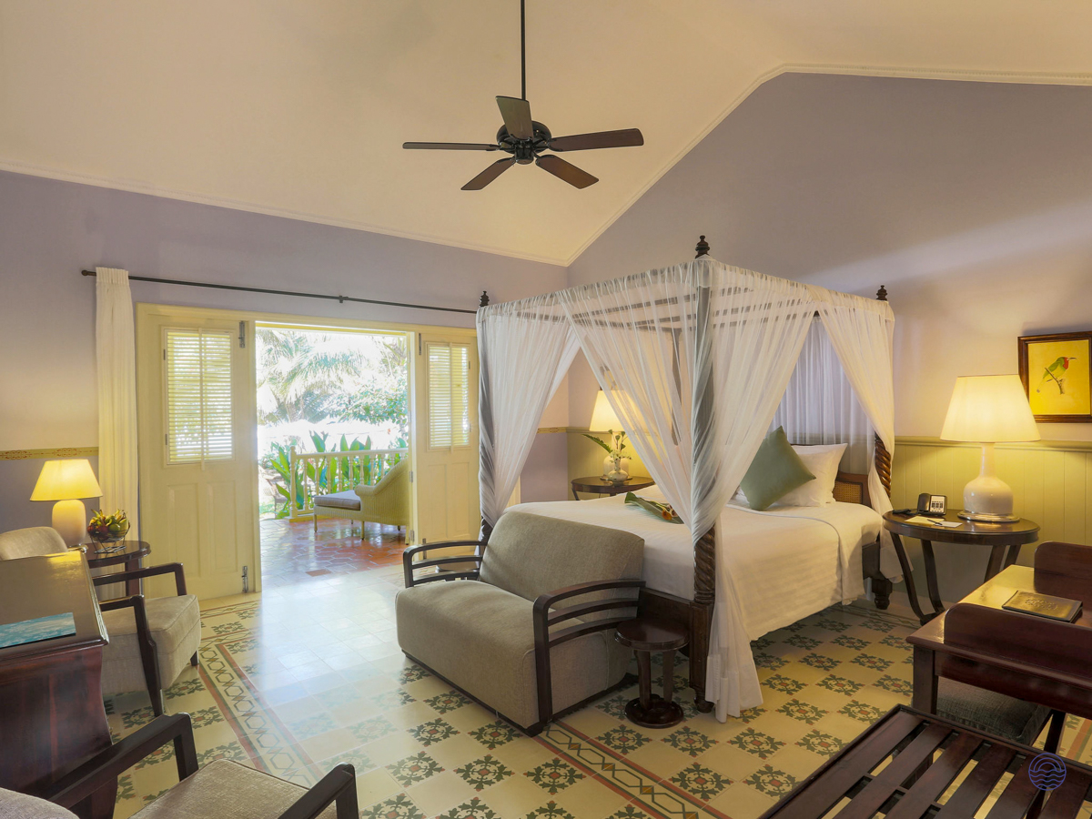 A luxurious hotel room in Phu Quoc with a four-poster bed and a balcony overlooking lush greenery.