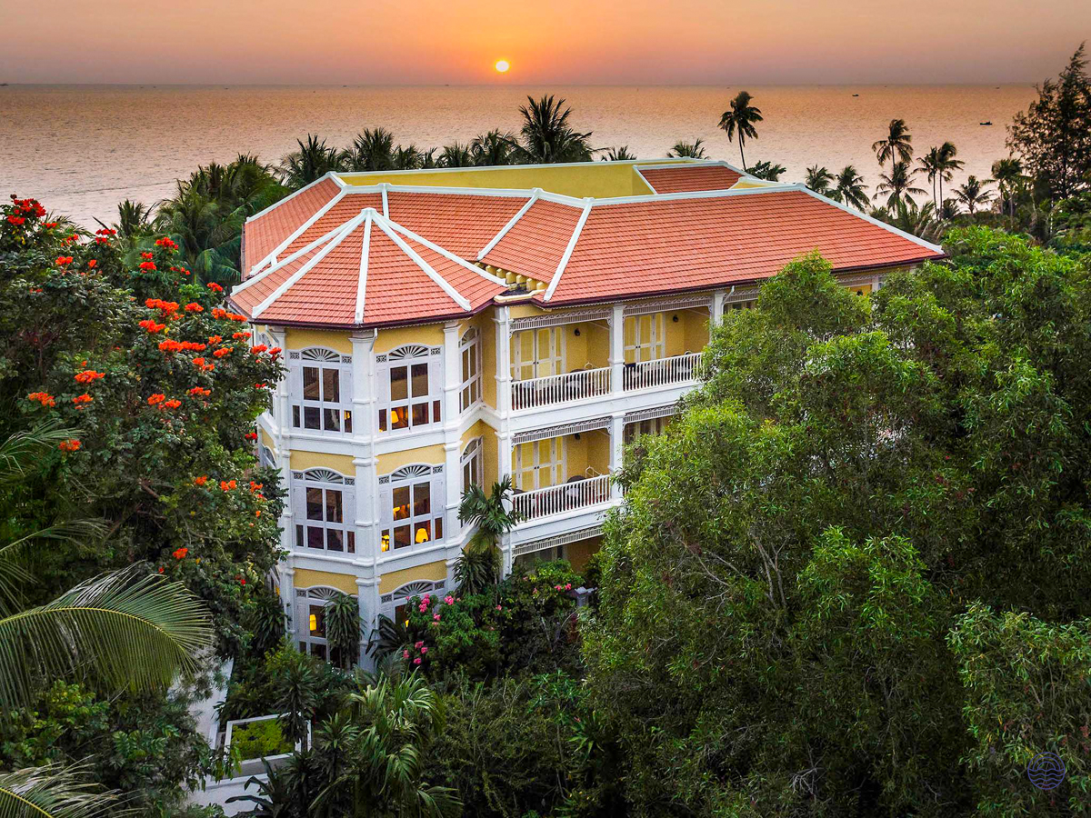 Elegant yellow and white hotel with a red roof surrounded by lush greenery at sunset in Phu Quoc.