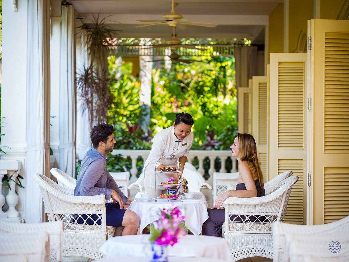 A couple enjoys afternoon tea served by a smiling waiter on a luxurious veranda in Phu Quoc.