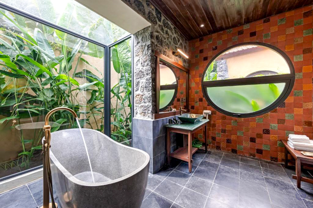 Luxurious bathroom at Tam Coc Retreat, featuring a stone tub and large windows overlooking lush gardens.