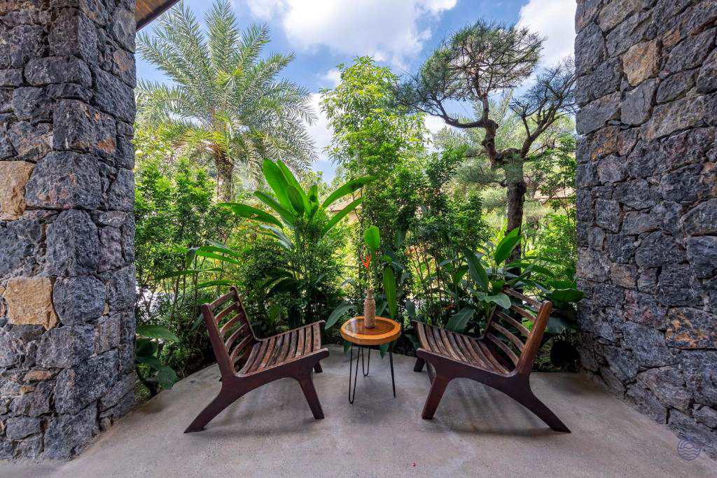 A tranquil patio with two wooden chairs and a small table, surrounded by lush tropical gardens in Tam Coc.