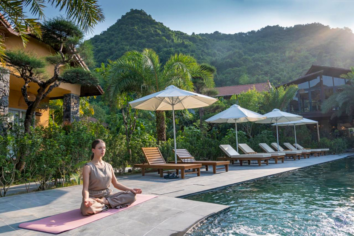 Woman meditating by a serene resort pool, surrounded by lush tropical gardens and mountains in Tam Coc.